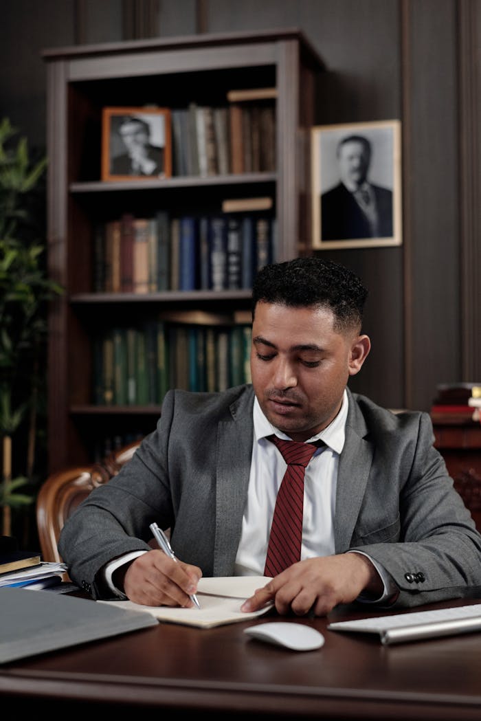A professional lawyer in a suit sits at a wooden desk in a well-decorated office.